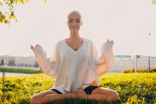 Portrait of young millenial european short haired woman doing yoga lotus asana on green grass meadow summer park sunset. Beautiful happy blonde girl outdoor.
