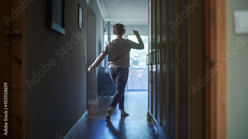 Happy Young Woman Wearing Headphones Dances Through Her Apartment Hallway. Back View Shot of Cheerful Girl Listening Music in a Good Mood.