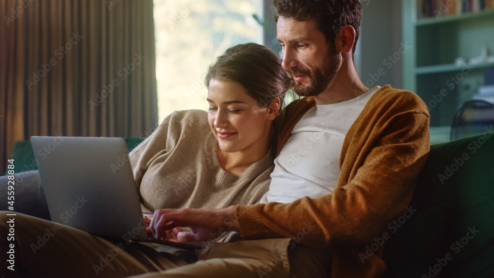 Young Couple Use Laptop Computer, while Sitting on a Couch in the Cozy Stylish Apartment. Boyfriend and Girlfriend Shopping on Internet, Using Social Media, Watching Funny Videos and Streaming Service Young Couple Use Laptop Computer, while Sitting on a Couch in the Cozy Stylish Apartment. Boyfriend and Girlfriend Shopping on Internet, Using Social Media, Watching Funny Videos and Streaming Service