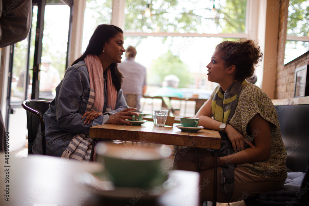 Young women friends talking and drinking cappuccinos at cafe table Young women friends talking and drinking cappuccinos at cafe table