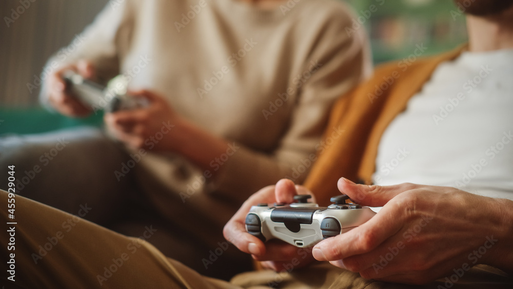 Happy Couple Sitting on the Sofa Playing Video Games, Using Controllers.  Competitive Girlfriend and Boyfriend in Love have Fun Playing in Online  Video Games at Home Together. Close-up Focus on Hands Stock