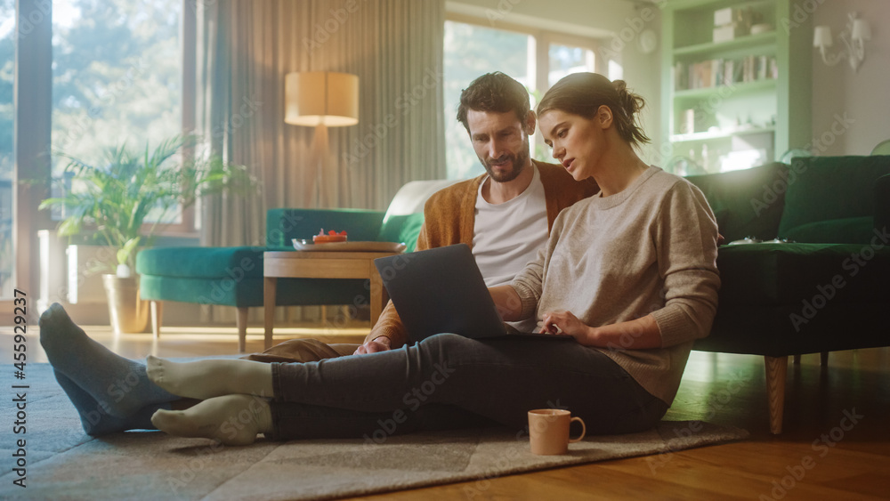 Couple Use Laptop Computer, while Sitting on the Living Floor room of their Apartment. Boyfriend and Girlfriend Talk, Shop on Internet, Choose Product to Order Online, Doing Remote Work Together Couple Use Laptop Computer, while Sitting on the Living Floor room of their Apartment. Boyfriend and Girlfriend Talk, Shop on Internet, Choose Product to Order Online, Doing Remote Work Together