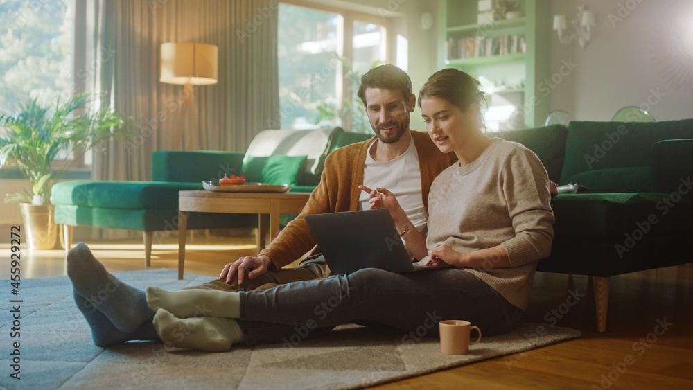 Couple Use Laptop Computer, while Sitting on the Living Floor room of their Apartment. Boyfriend and Girlfriend Talk, Shop on Internet, Choose Product to Order Online, Doing Remote Work Together Couple Use Laptop Computer, while Sitting on the Living Floor room of their Apartment. Boyfriend and Girlfriend Talk, Shop on Internet, Choose Product to Order Online, Doing Remote Work Together