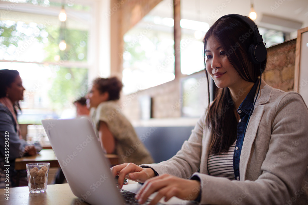 Young woman with headphones using laptop at cafe table Young woman with headphones using laptop at cafe table