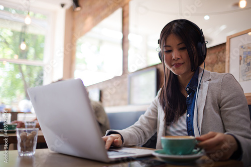 Young woman with headphones using laptop at cafe table Free Download Young woman with headphones using laptop at cafe table - GFXLoad