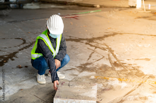 Young Asian female construction engineer wearing a medical mask to cover her mouth and wearing a white safety helmet concrete plinth inspection cut from the floor, in the construction zone, camera