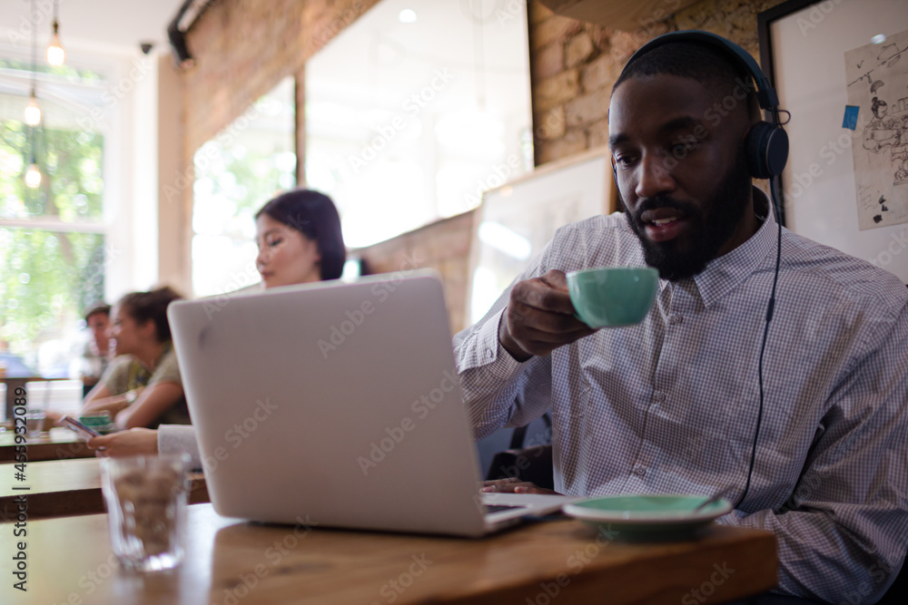 Man with headphones using laptop and drinking coffee in cafe Man with headphones using laptop and drinking coffee in cafe