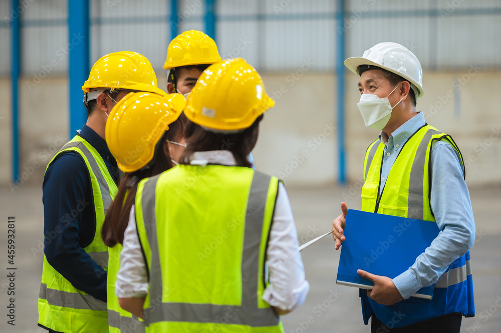 The factory employee consists of engineers, foreman, technicians, and related department staff. Wear a mask, hard hat, and vest. meeting before starting work inside the warehouse. Teamwork concept.
