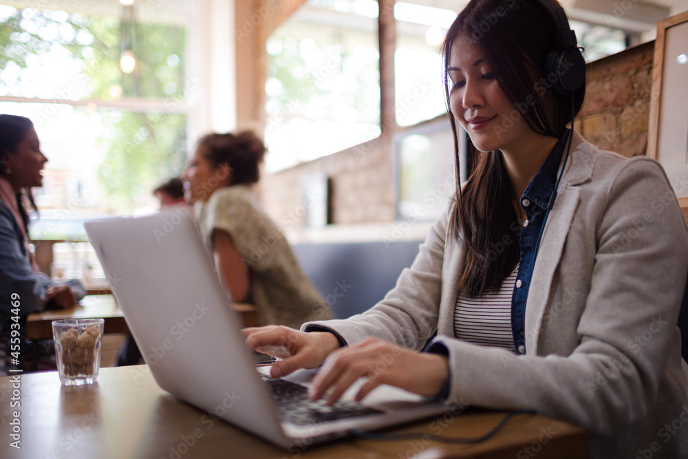 Young woman with headphones using laptop at cafe table