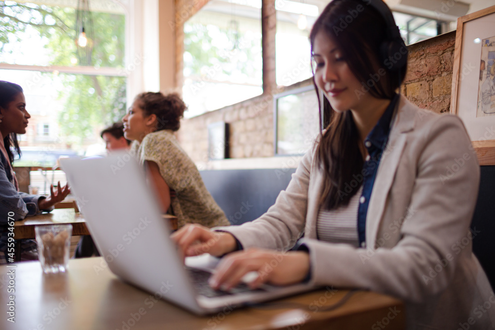Young woman with headphones using laptop at cafe table Young woman with headphones using laptop at cafe table