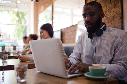 Man with headphones using laptop and drinking coffee in cafe