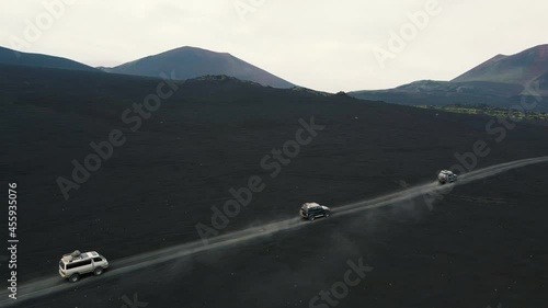 Three offroad vehicles driving along the wild road in volcanic desert pan aerial view. Extreme tourism at Kamchatka, Russia. photo