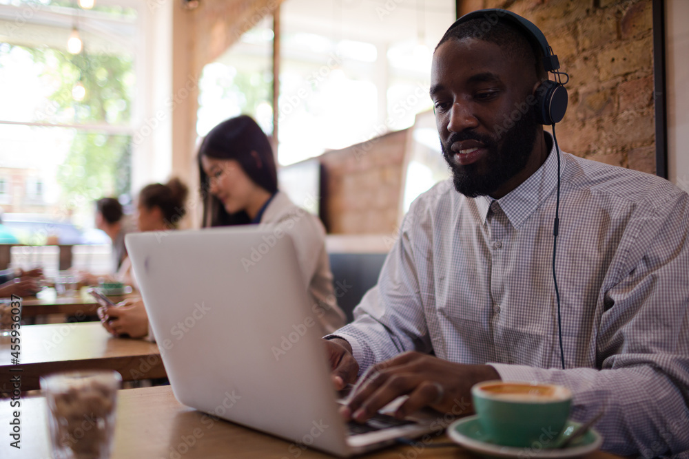 Man with headphones using laptop and drinking coffee in cafe Man with headphones using laptop and drinking coffee in cafe
