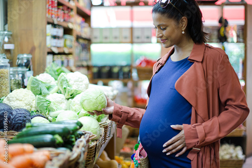Pregnant woman shopping for cabbage in grocery store