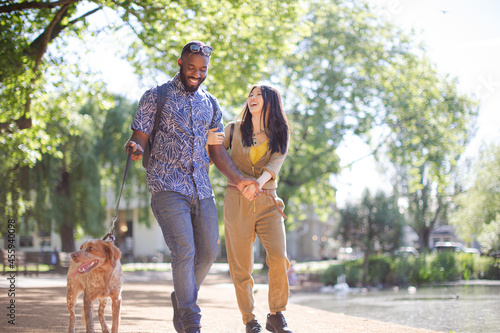 Happy young couple walking dog in sunny park photo