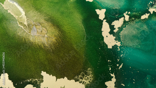 Abstract emerald, gold ink spreads in waves, close-up. Rich light aqua green. Texture of golden islets on ink green tide. Sparkling gold sequins in ink spreads, seethes. Foto of sparkling paint