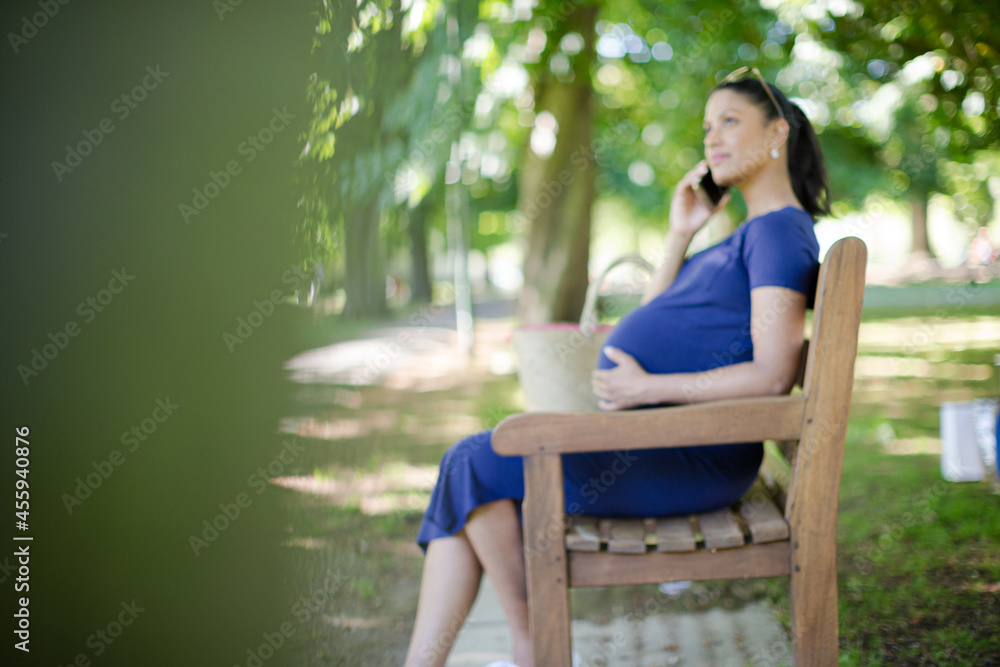 Pregnant woman talking on cell phone on park bench Pregnant woman talking on cell phone on park bench