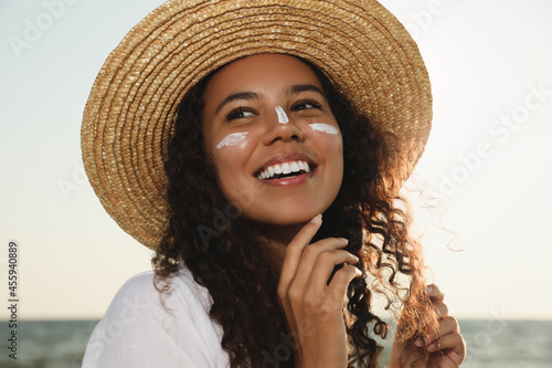 Happy African American woman with sun protection cream on face near sea