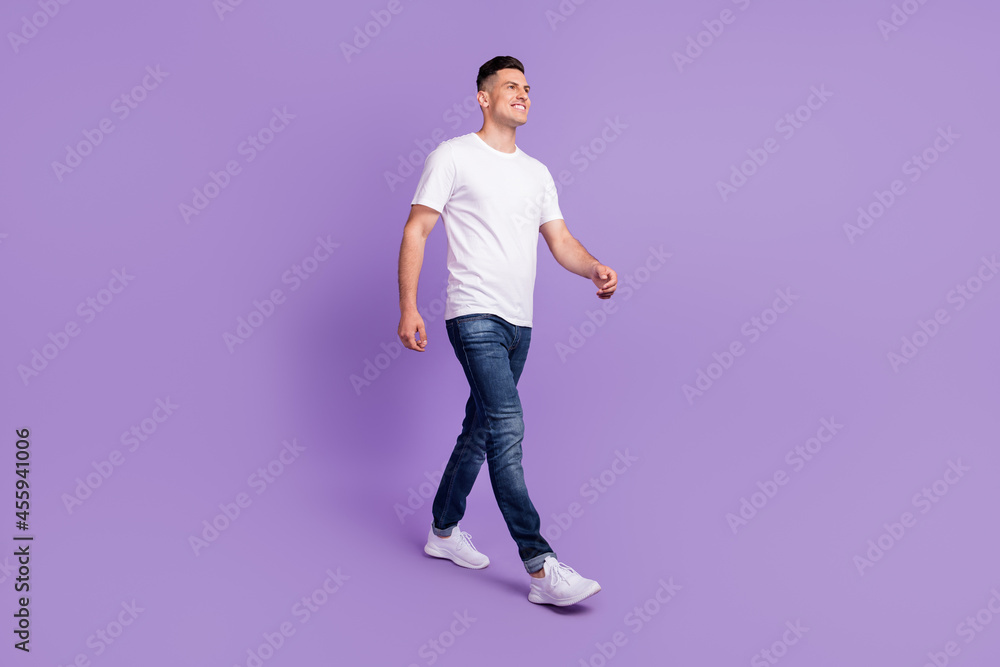 Full body photo of charming positive cheerful man look walk empty space smile isolated on purple color background