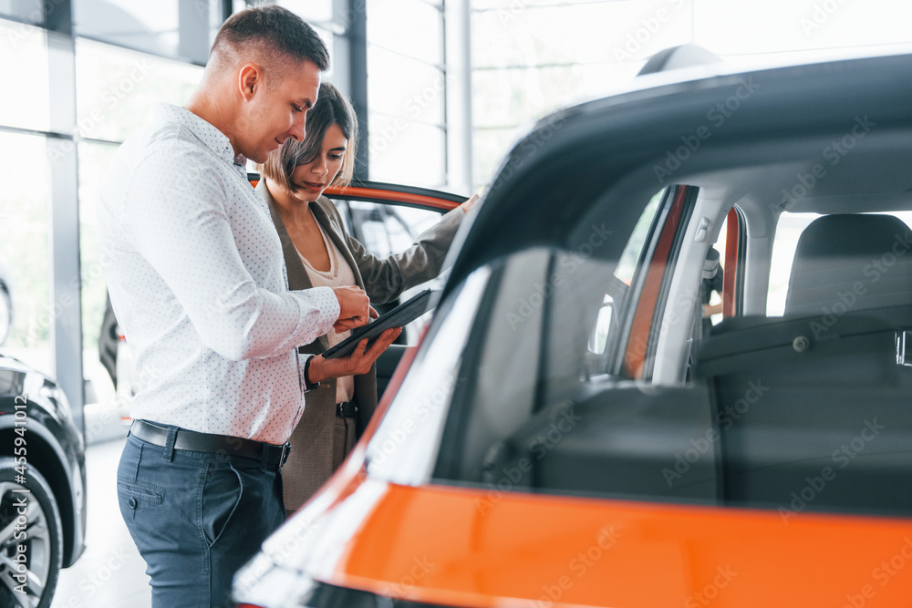 Information document in hands. Man in formal wear helping customer with choice of the automobile Information document in hands. Man in formal wear helping customer with choice of the automobile