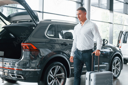 Conception of tourism. Man in formal clothes is with luggage indoors near the car © standret
