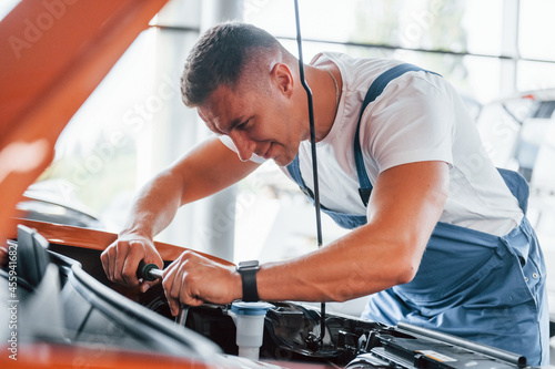 Man in uniform is repairing broken automobile indoors