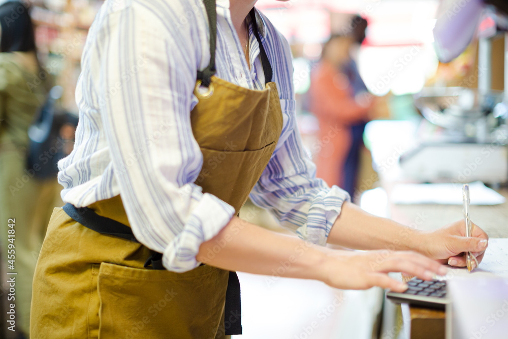 Fototapeta premium Female cashier using calculator in grocery store
