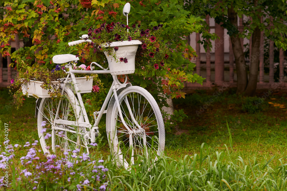 The white bicycle in the garden is decorated with flowers. Blurred background.
