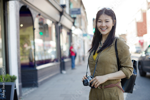 Portrait smiling, confident young female tourist with camera on sunny urban street