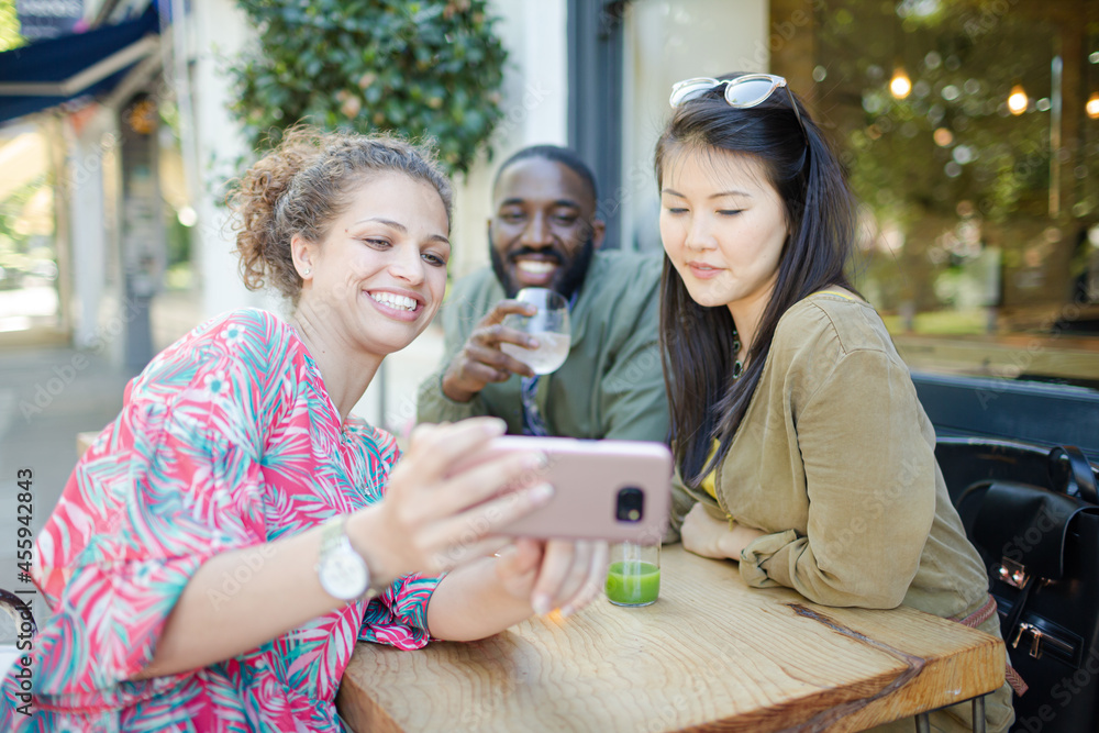 Smiling young friends taking selfie with camera phone at sidewalk cafe