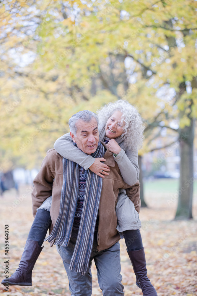 Fototapeta premium Senior man carrying woman on his back in autumn park