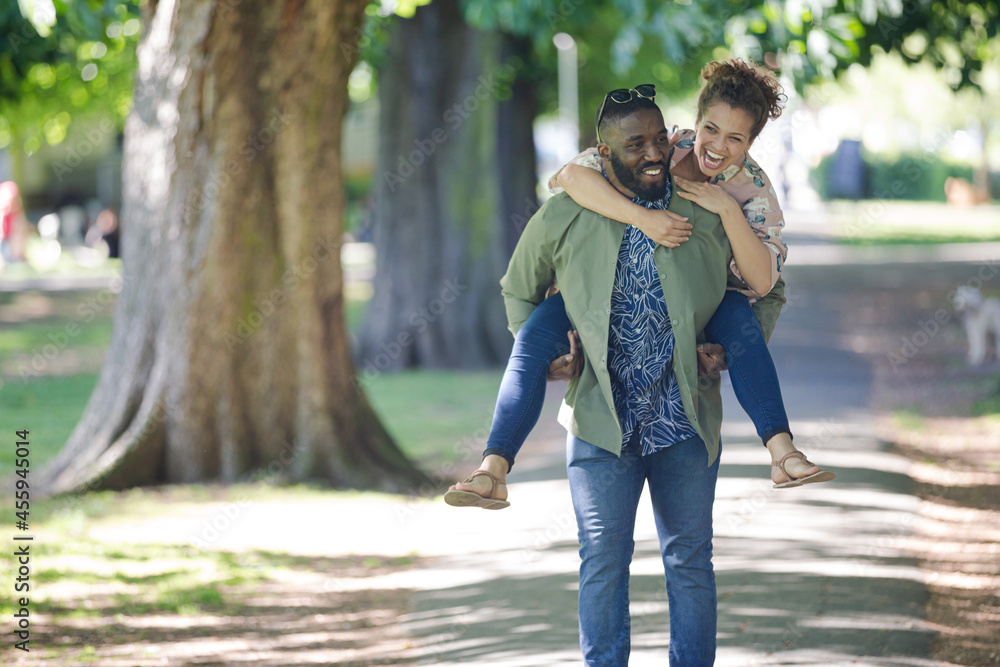 Playful young couple piggybacking in park Playful young couple piggybacking in park