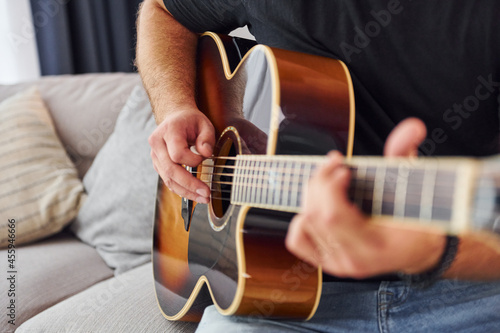 Playing the instrument. Man in casual clothes and with acoustic guitar is indoors