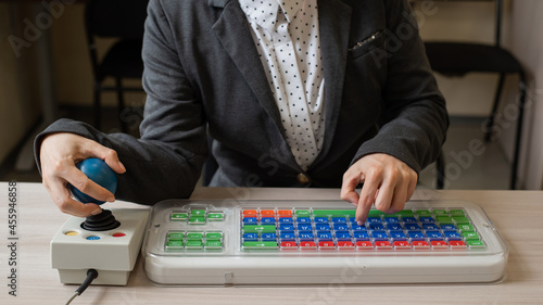 An unrecognizable woman with cerebral palsy is typing on the keyboard. A girl with disabilities works on a specially equipped computer
