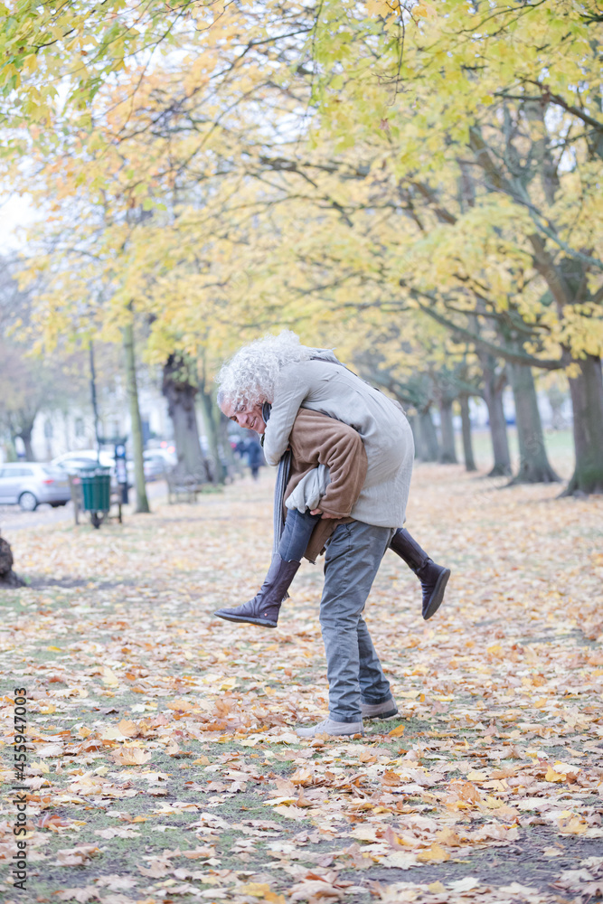 Fototapeta premium Senior man carrying woman on his back in autumn park
