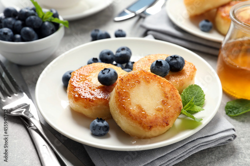 Delicious cottage cheese pancakes with blueberries, mint and honey on light grey table, closeup © New Africa