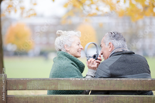 Happy senior couple sharing headphones, listening to music in park © KOTO