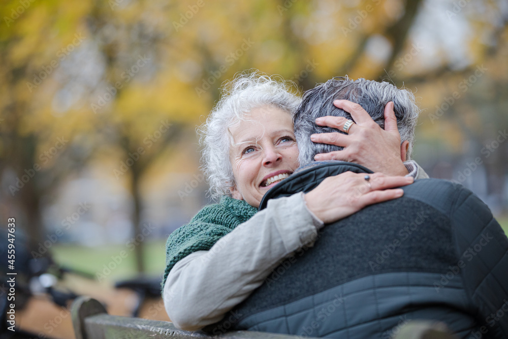 Fototapeta premium Smiling, affectionate senior couple hugging on bench in autumn park