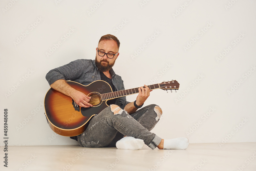 Obraz premium In the studio. Man in casual clothes and with acoustic guitar is indoors