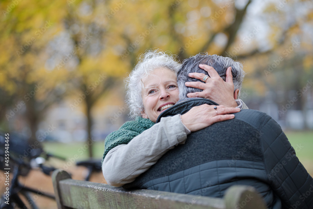 Smiling, affectionate senior couple hugging on bench in autumn park Smiling, affectionate senior couple hugging on bench in autumn park