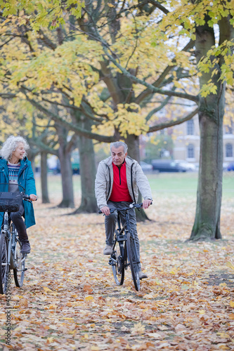 Senior couple bike riding among trees and leaves in autumn park