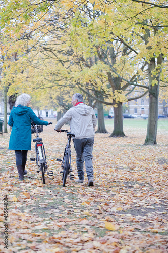 Senior couple walking bicycles among trees and leaves in autumn park © KOTO