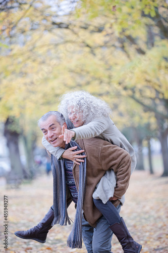 Senior man carrying woman on his back in autumn park