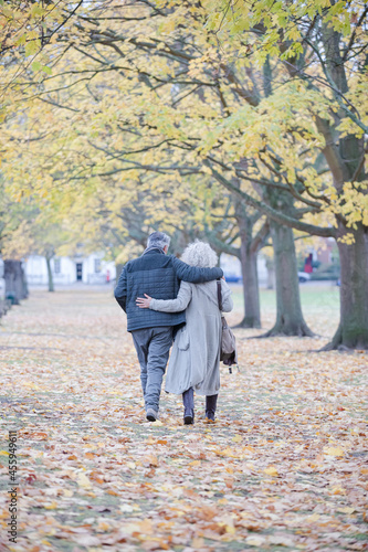 Affectionate couple hugging, walking among trees and leaves in autumn park