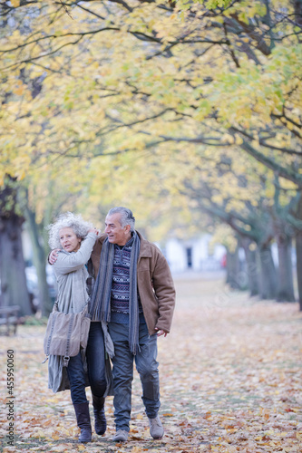 Affectionate couple hugging, walking among trees and leaves in autumn park