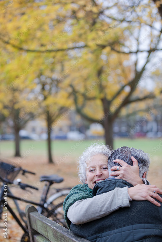 Smiling, affectionate senior couple hugging on bench in autumn park Smiling, affectionate senior couple hugging on bench in autumn park