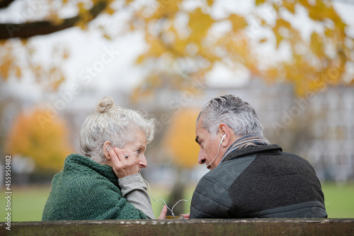 Happy senior couple sharing headphones, listening to music in park © KOTO
