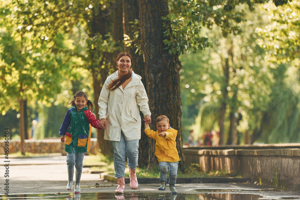 Obraz premium Front view. Mother with her little son and daughter have a walk outdoors in the park after the rain