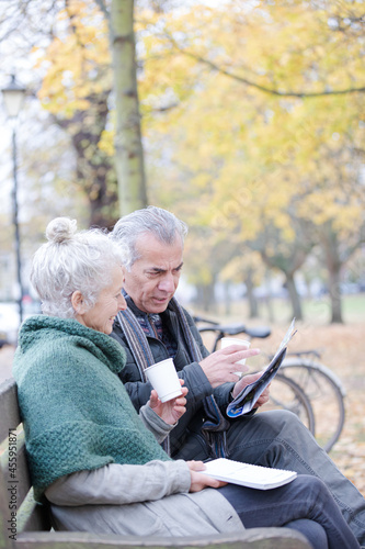 Senior couple reading newspaper and drinking coffee on bench in autumn park © KOTO