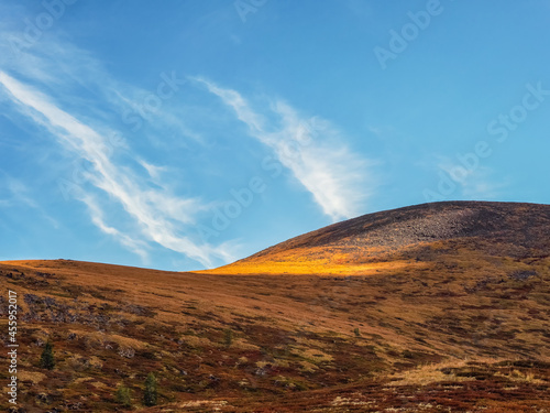 Minimalistic beautiful mountain scenery with golden light on slopes mountains. Scenic mountain landscape with illuminating color in blue sky.